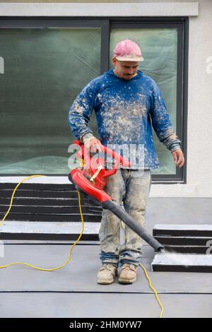 Santa Clara, California - November 14, 2029: Construction worker with blower cleaning off debris from a rooftop. Stock Photo
