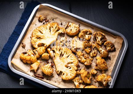 Food concept Roasted organic Cauliflower in baking tray on black slate stone background with copy space Stock Photo