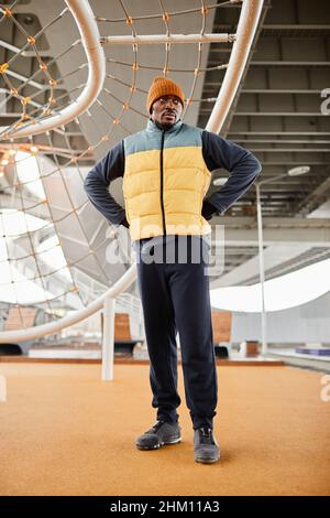 Young serious African American athlete standing on sports ground with facilities against rope net for pulling up and crowling Stock Photo