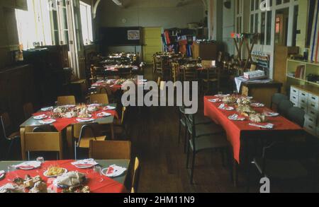 1977, historical, inside a village primary school, sandwiches and cakes on tables with red tablecloths, prepared for the children to sit down together to celebrate the Silver Jubilee of Her Majesty, Queen Elizabeth II, England, UK. Stock Photo