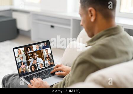 Cropped view of the multiracial man in casual wear sitting on the comfortable sofa and using trendy laptop for video call with many interlocutor. Virtual meeting, video call concept Stock Photo