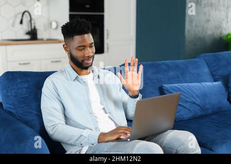 Video call. Cheerful attractive multiracial guy using computer app for video communication. Smiling guy looking and waiving into the camera, greeting, talking online Stock Photo