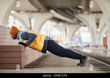 Young African American athlete doing push ups against brick step while exercising on sports ground during outdoor workout Stock Photo