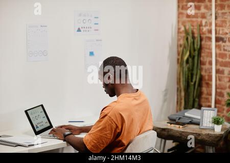 Contemporary young male economist analyzing financial data on lapto pscreen while sitting by desk in openspace office Stock Photo