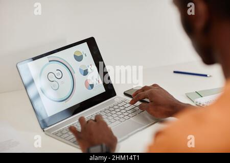 African American male economist or accountant sitting in front of laptop with financial data on screen and analyzing diagrams Stock Photo
