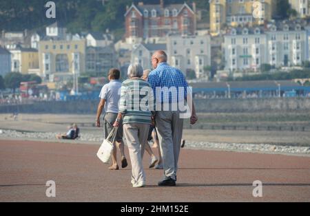ELDERLY COUPLE WALKING ON THE SEAFRONT AT LLANDUDNO NORTH WEST WALES RE EXERCISE FITNESS HEALTH HEALTHY LIFESTYLE PENSIONERS PENSIONS ETC UK Stock Photo
