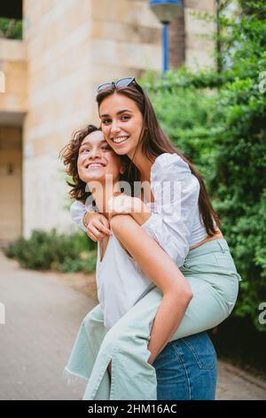 Happy young woman giving her friend a piggy back ride in the city Stock Photo