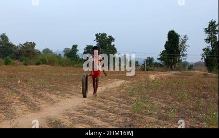 A boy playing with a motor cycle tyre in a rural village. Javadhu Hills, Tamil Nadu. India. Stock Photo