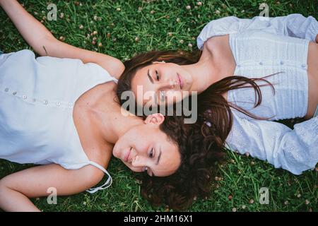 Two relaxed girls laying down on the grass in a park while they are resting Stock Photo