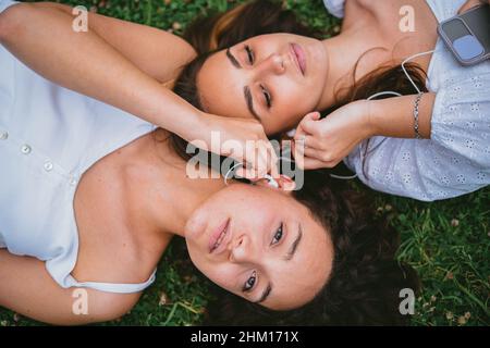 Two relaxed teenagers listening to music on earbuds. They are taking a break from classes. Stock Photo