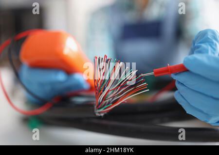 Hands with a voltmeter check colored wires in the cable, blurry Stock Photo