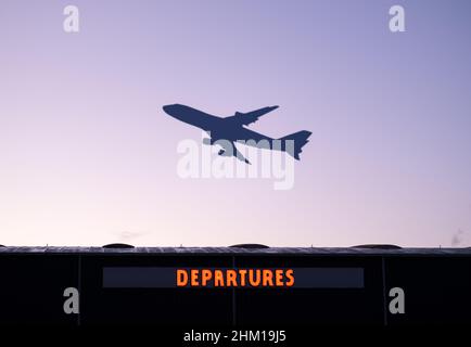 An Airplane Taking Off At Sunset With The Airport Departures Building In The Foreground Stock Photo