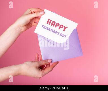Hands putting card with happy Valentines day greeting in envelope. Celebration postcard on pink background. High quality photo Stock Photo