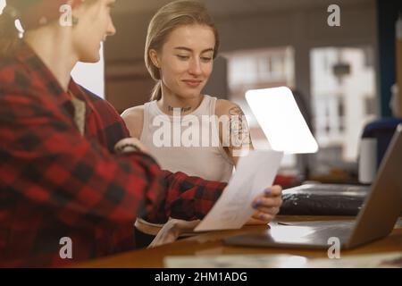 Tattoo master helping client to choose pattern in her salon Stock Photo
