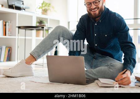 Cheerful Entrepreneur Man Using Laptop Writing Taking Notes At Home Stock Photo