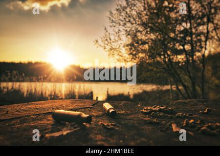 hunting ammunition lies on a wooden table by the lake at sunset Stock Photo