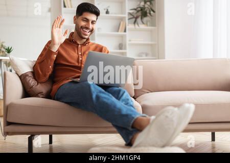 Smiling man working on laptop waving hand Stock Photo