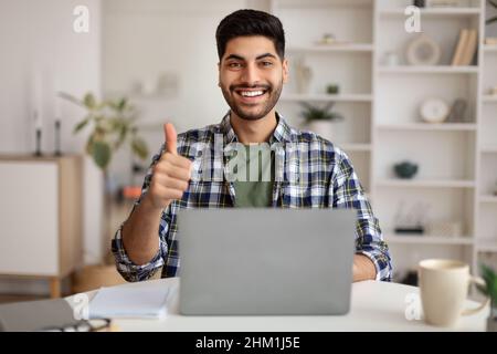 Portrait of smiling Arab man using laptop showing thumbs up Stock Photo