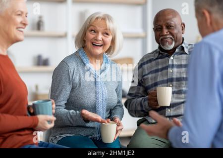 Multiracial group of positive elderly people drinking tea, chatting Stock Photo