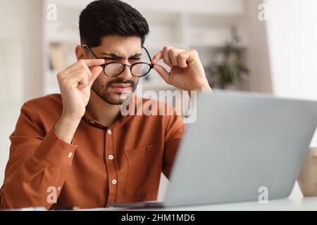 Confused Arab guy using laptop looking at screen Stock Photo