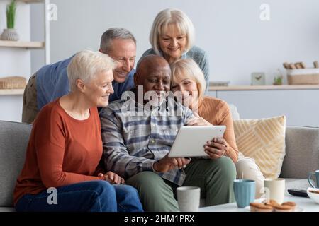 Happy elderly people spending time together at home, using gadgets Stock Photo