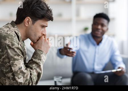 Depressed young man soldier visiting black psychologist Stock Photo