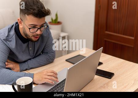 Young guy doing internet research on his computer for his online classes with his coffee, tablet and mobile phone on the table. Stock Photo