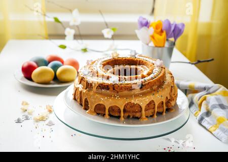 Delicious Easter cake on kitchen table with colored eggs and handmade paper flowers. Easter breakfast. Holidays concept Stock Photo