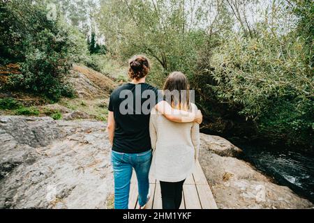 A back view shot of a young couple taking a walk near the river over a wooden path Stock Photo
