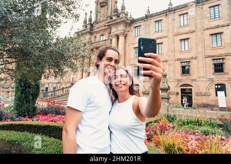 A young couple taking a fancy selfie in a garden in front of an old building Stock Photo