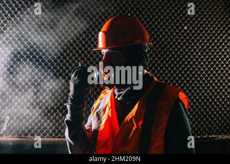 Man in respirator talking on walkie-talkie during fire in industrial building. Stock Photo