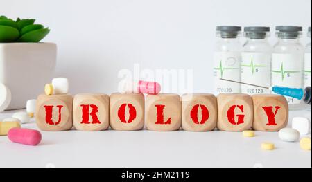 Word UROLOGY. Urology text on wooden blocks. In front of a row of cubes are ampoules, in the background - white plastic packaging from tablets, the cu Stock Photo