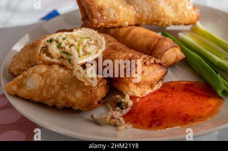 A plate of whole and cut crispy spring rolls showing the vegetable and meat fillings, dipping sauce and spring onions. Stock Photo