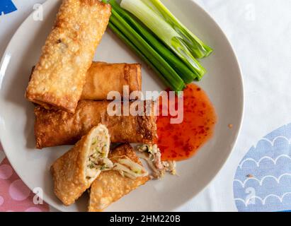 Whole and cut crispy fried spring rolls served on a plate with green onions and Thai sweet chilli sauce. Stock Photo