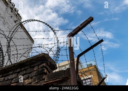 A barb wire fence on top of a brick wall. Stock Photo