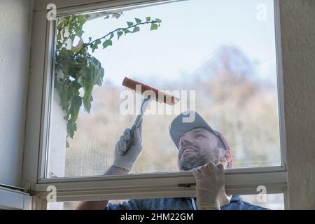 young man is using a rag and squeegee while cleaning windows. professional window cleaner Stock Photo