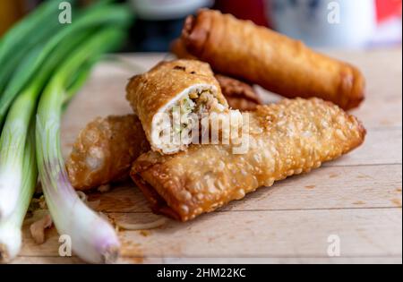 Half cut and whole crispy fried spring rolls on a wooden board with spring onions ready for serving. Stock Photo
