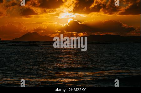 A massive sunset between the clouds with some islands over the ocean Stock Photo