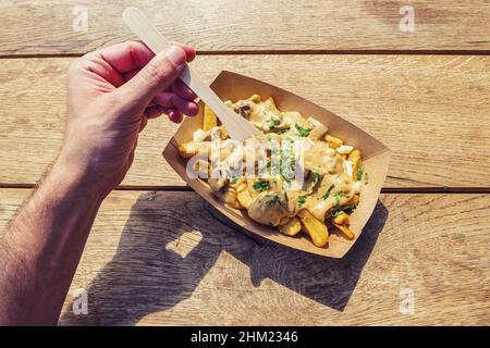 Man hold a fork to eat ench fries with mushrooms sauce on a wooden table, point of view shot. Stock Photo