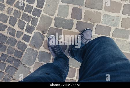 Young man standing in at the street in a oldtown in casually dressed sneakers, Point of view shot Stock Photo