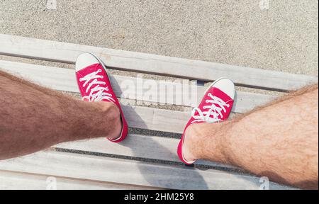 Young man in Red Sneakers sits on a bench at a summer day, Point of view shot Stock Photo