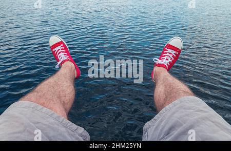 Mens legs in sneakers in background of a sea landscape Summer Beach Relaxing Concept, Point of view shot Stock Photo