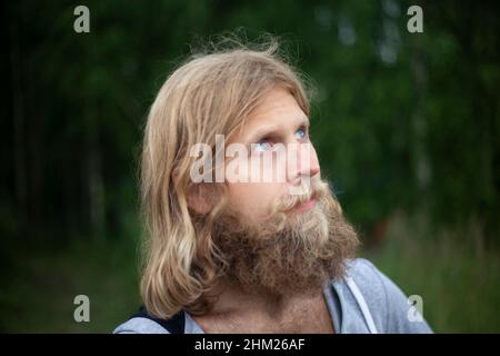 Guy with thick unshaved beard. Young man in white hoodie. Man in nature. Portrait of traveler. Stock Photo