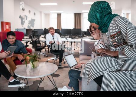 Multiethnic startup business team having brainstorming in relaxation area of modern office interior working on laptop and tablet computer Stock Photo