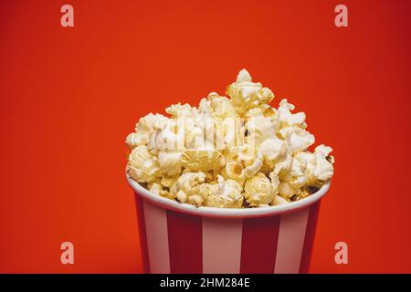 Popcorn in a round box and around on a bright red background. Stock Photo