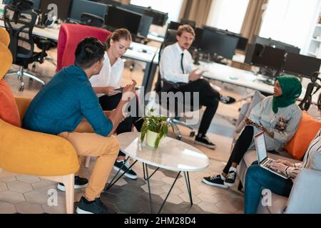 Multiethnic startup business team having brainstorming in relaxation area of modern office interior working on laptop and tablet computer Stock Photo
