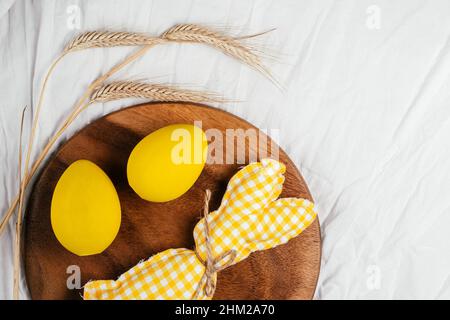 Easter postcard for celebration holiday, one handmade square brown, white and yellow colored bunny with string-scarf on white gray textile background, Stock Photo