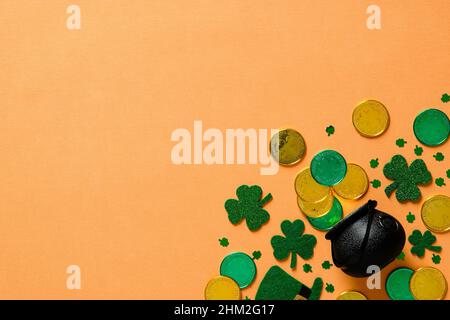 St Patricks Day banner design with pot of gold, shamrock clover leaves on orange background. Flat lay, top view, copy space. Stock Photo