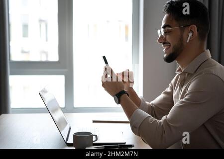 Relaxed smiling man using phone sitting front of laptop computer at home office Stock Photo