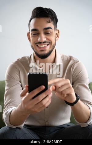 Happy young man laughing looking at cell phone sitting in living room at home Stock Photo